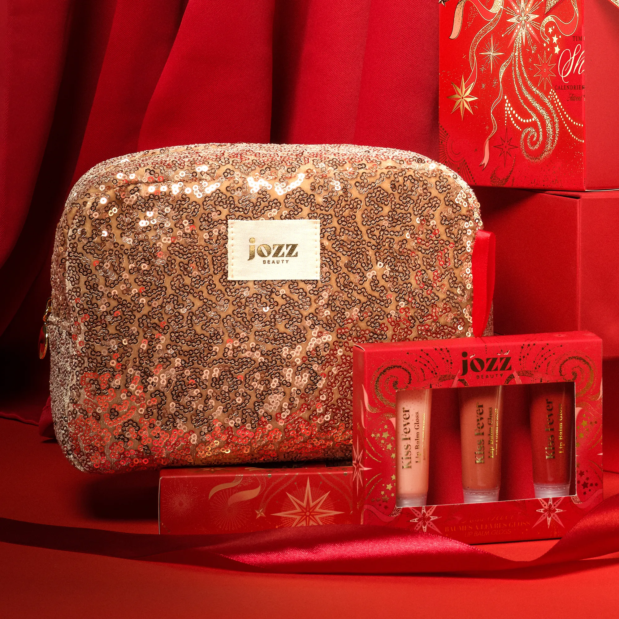 Grande trousse de toilette à sequins JOZZ Beauty posée avec un coffret Kiss Fever dans un décor de Noël rouge