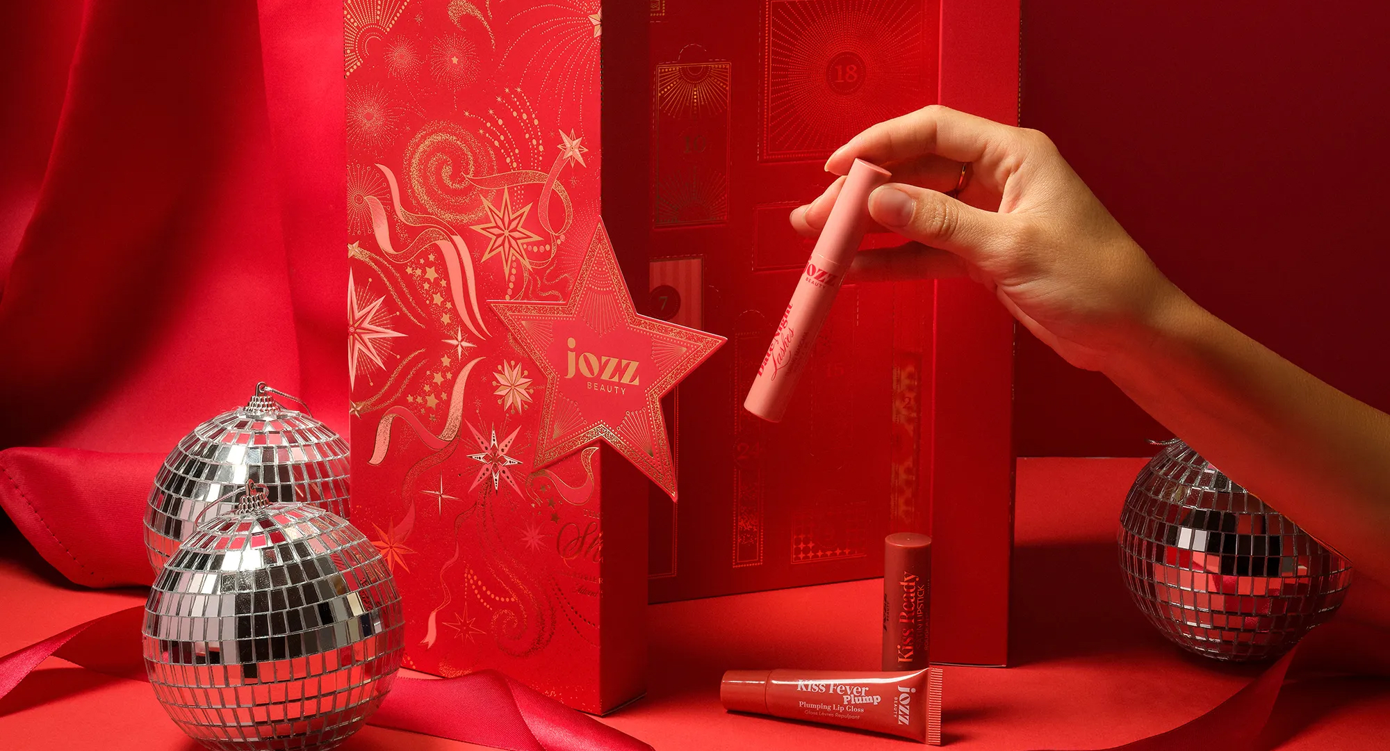 Mise en scène de Noël réunissant le Calendrier de l’Avent rouge Time To Shine et plusieurs coffrets JOZZ Beauty sur fond rouge